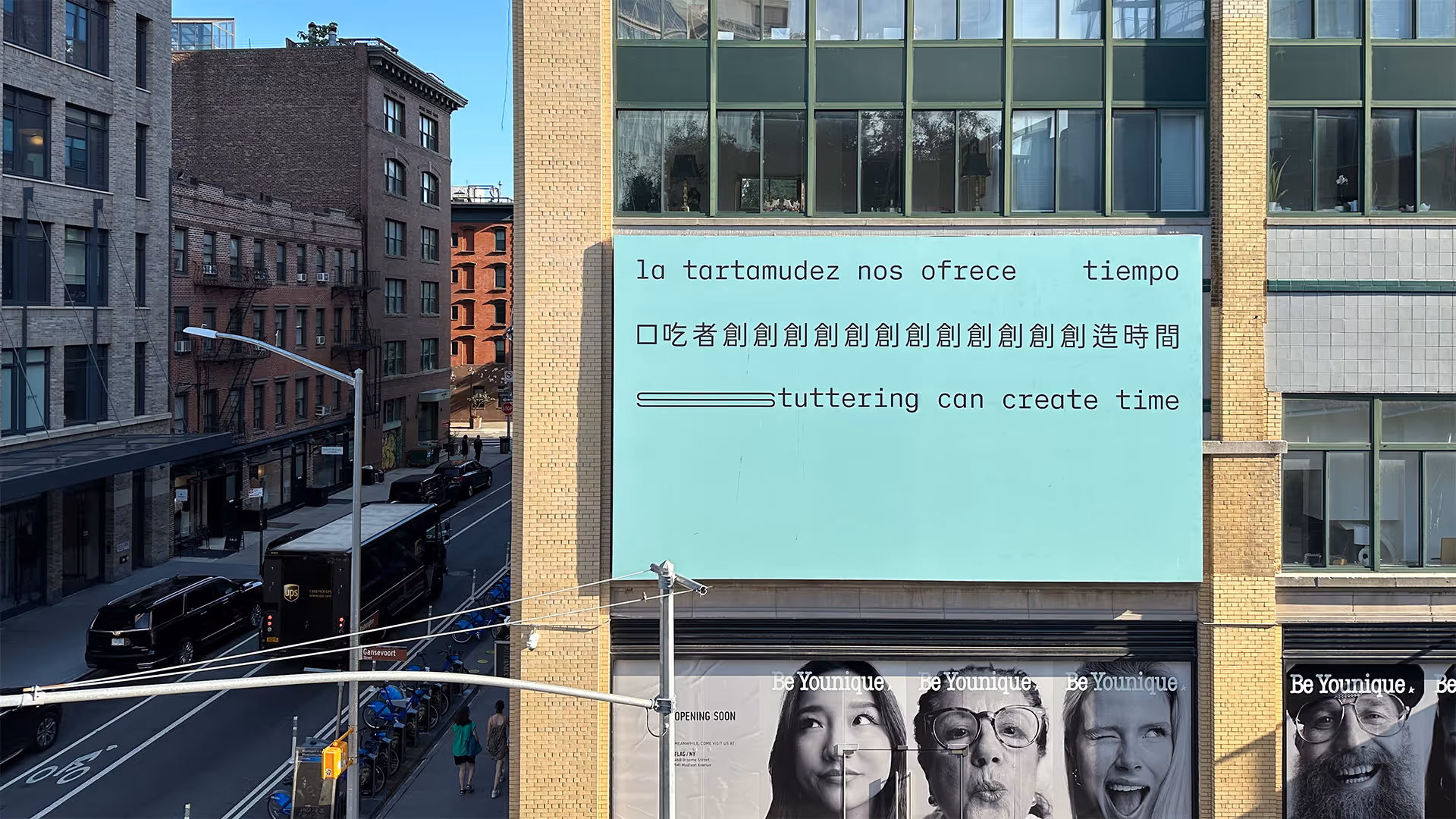 A billboard on a New York City building. Three lines of black text appear on a light seafoam green background, in Spanish, Chinese and English, translating to: ‘Stuttering can create time.’ The text is in a sans serif typeface organized in three straight lines within the top half of the composition. The bottom half of the composition is empty. The text is stretched and repeated to represent stammering.