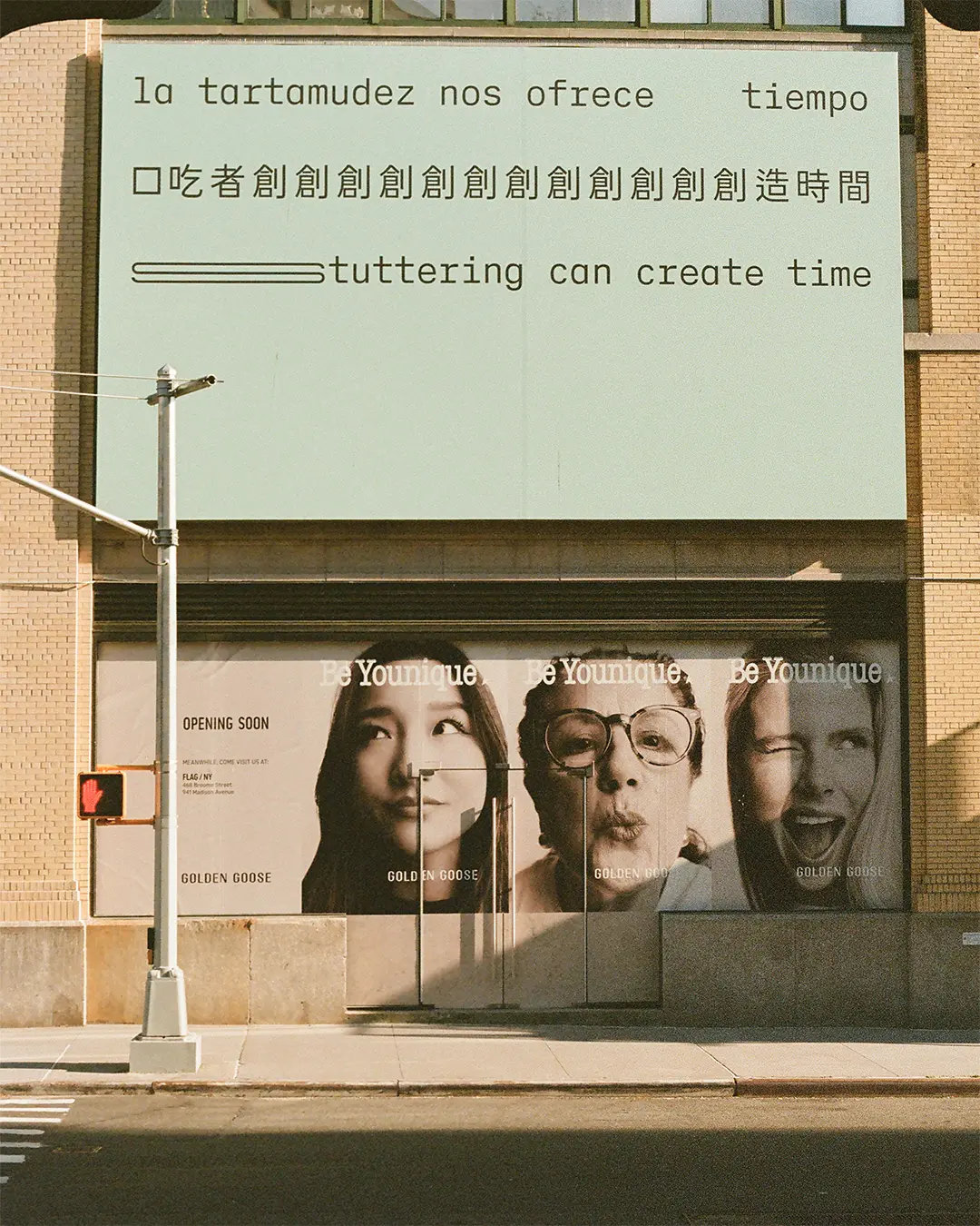A film photograph of a billboard. Three lines of black text appear on a light seafoam green background, in Spanish, Chinese and English, translating to: ‘Stuttering can create time.’ The text is in a sans serif typeface organised in three straight lines within the top half of the composition. The bottom half of the composition is empty. The text is stretched and repeated to represent stammering.