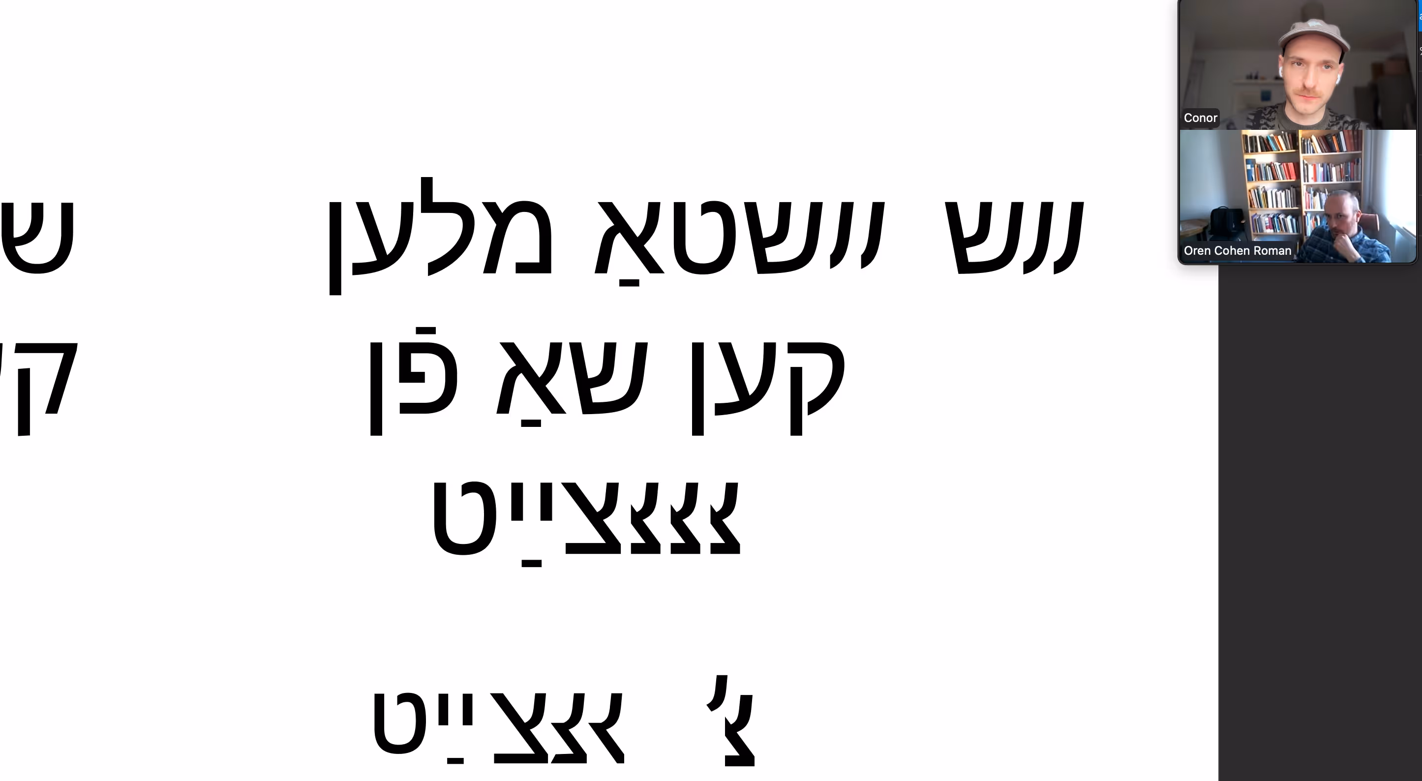 Screenshot of a video call between two men. In the centre of the frame is a white digital canvas with black typography in Yiddish.